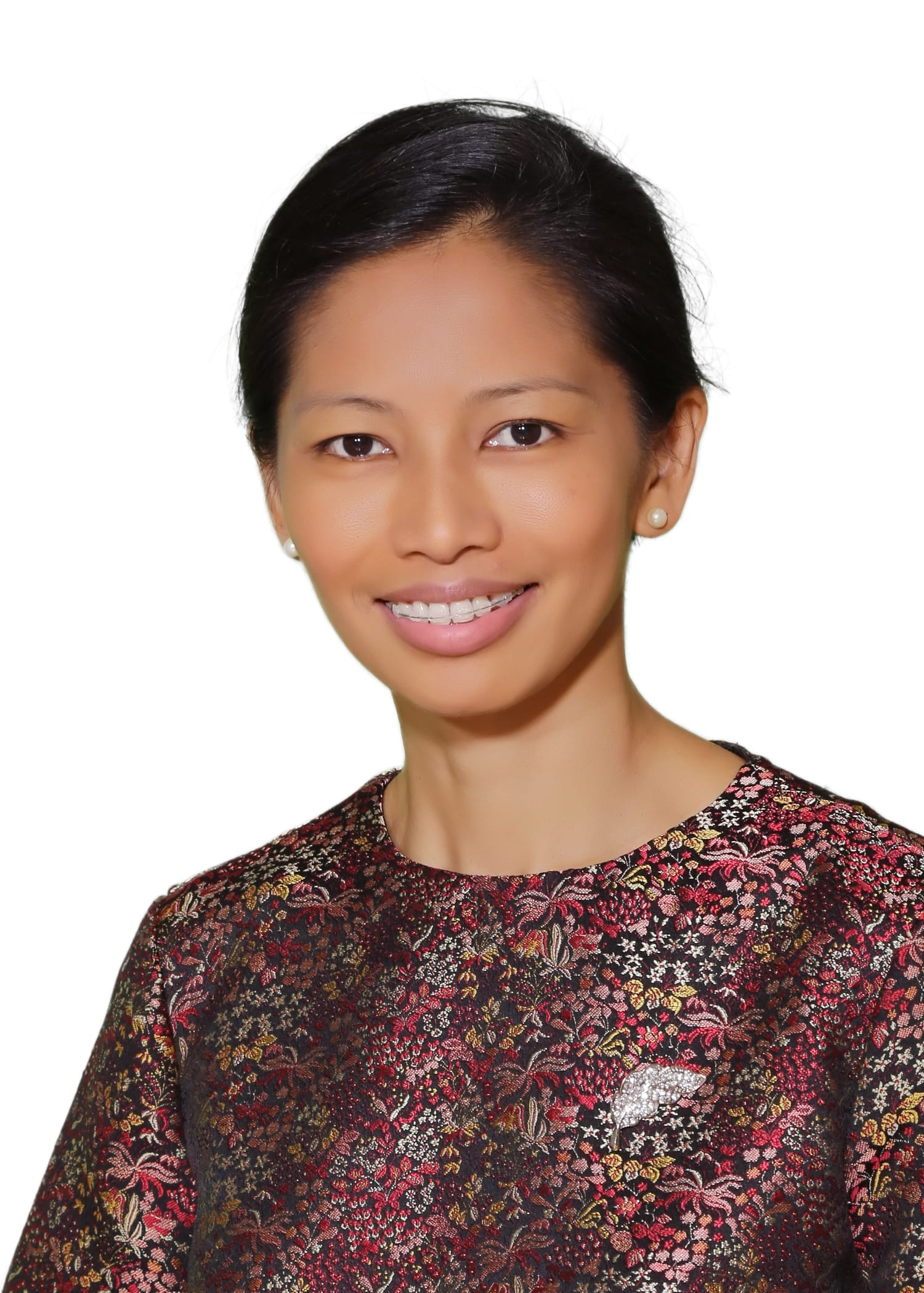 Woman with black hair pulled back, smiling, wearing pearl earrings and a dark floral patterned top, white background.